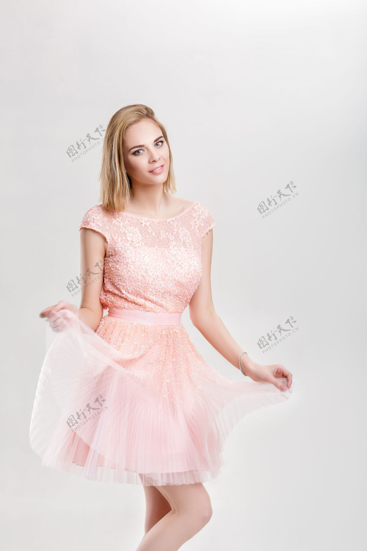 姿势美丽的金发性感女人穿着淡粉色的鸡尾酒裙 在灰色的背景下跳舞 玩得很开心浪漫服装工作室