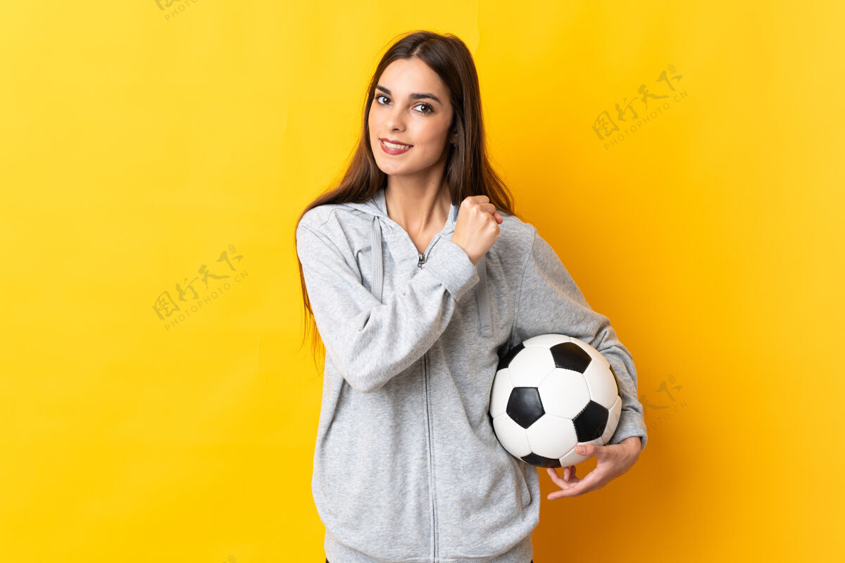 提高一个年轻的足球运动员 一个被隔离在黄色背景下庆祝胜利的女人比赛竞争年轻