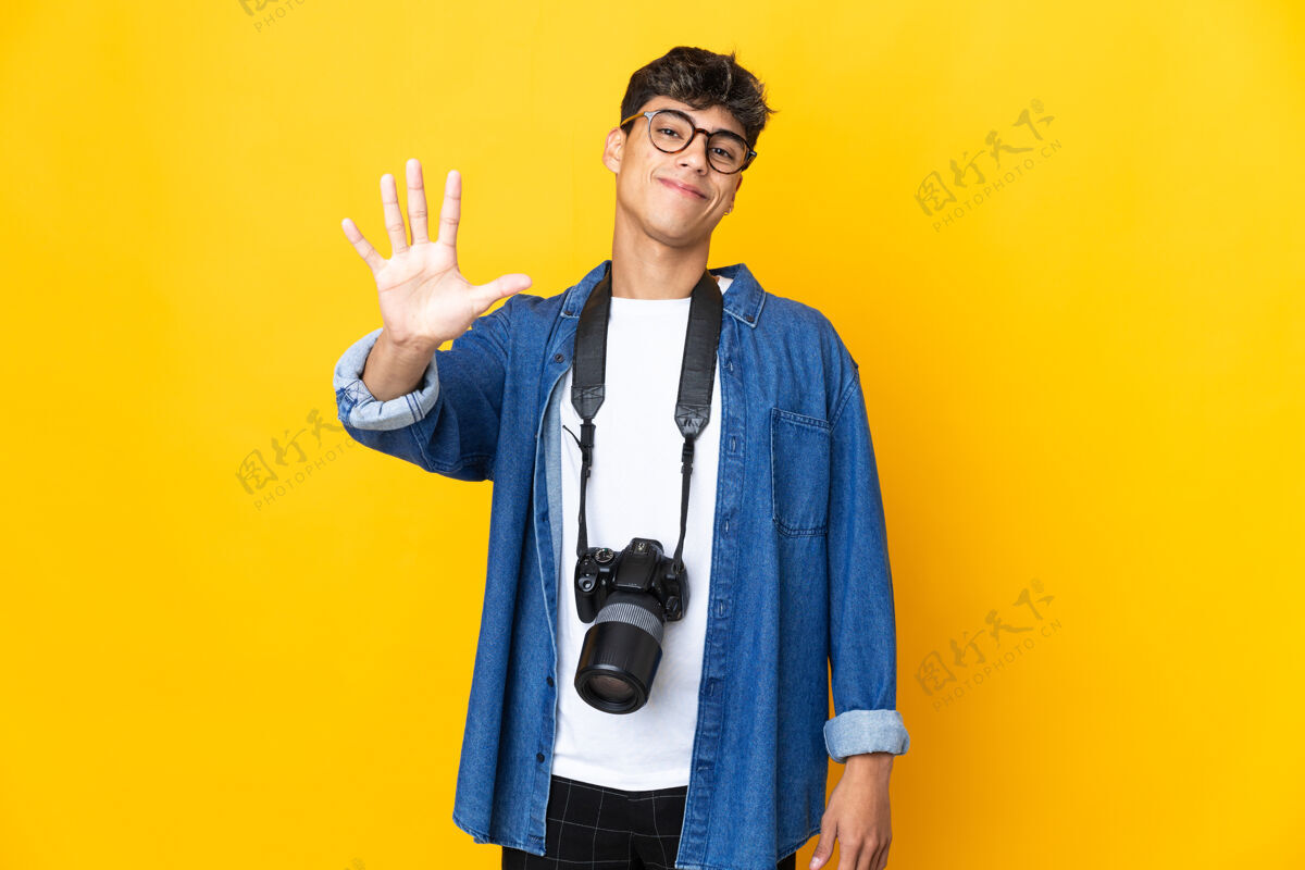 想法年轻的摄影师在孤立的黄色背景上用手指数到五男性五相机