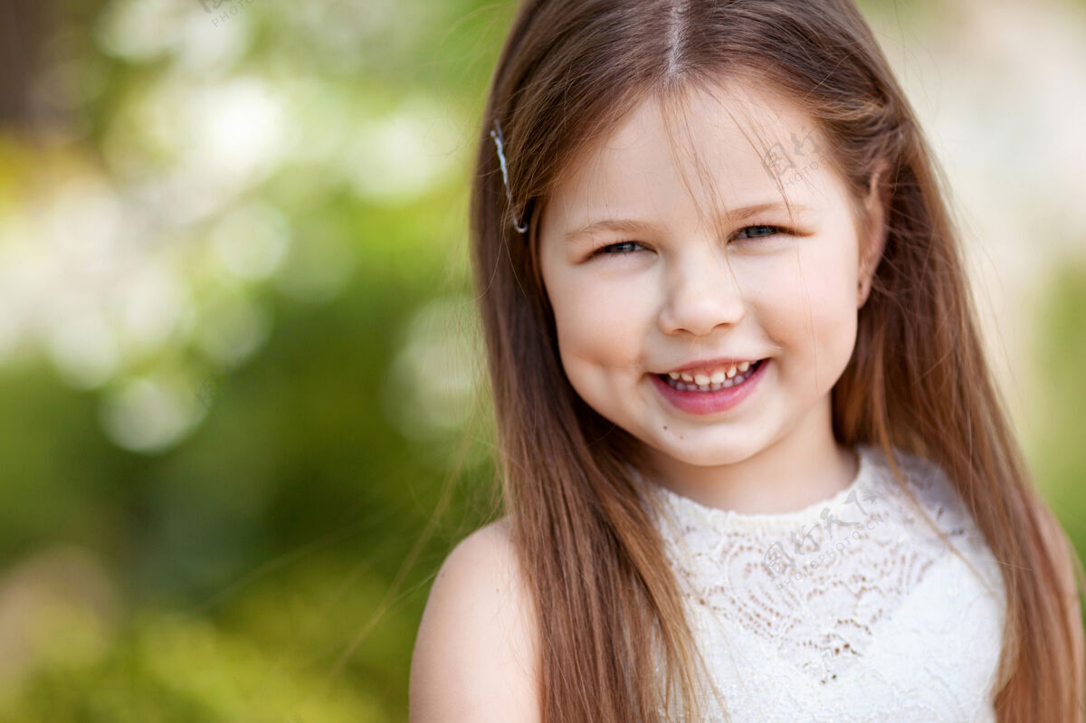 春天美丽微笑的小女孩穿着奶油色的裙子 映衬着夏日公园的绿色草可爱时尚
