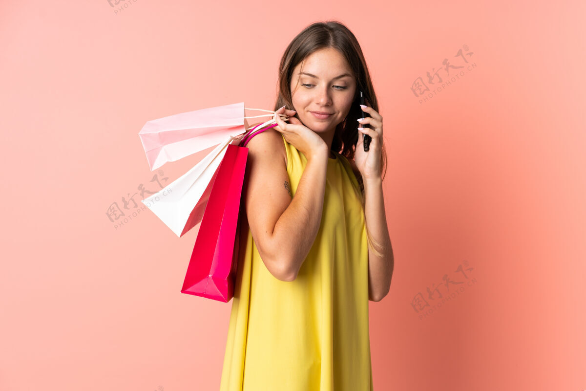 电话一位年轻的立陶宛妇女 手拿购物袋 拿着手机给朋友打电话 被隔离在粉色背景下手机商业购买