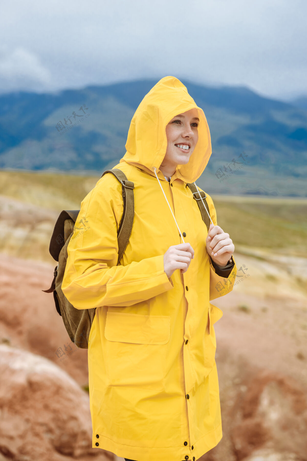 女孩带着背包的快乐女士穿着黄色夹克站在彩色山顶上岩石远足者背包