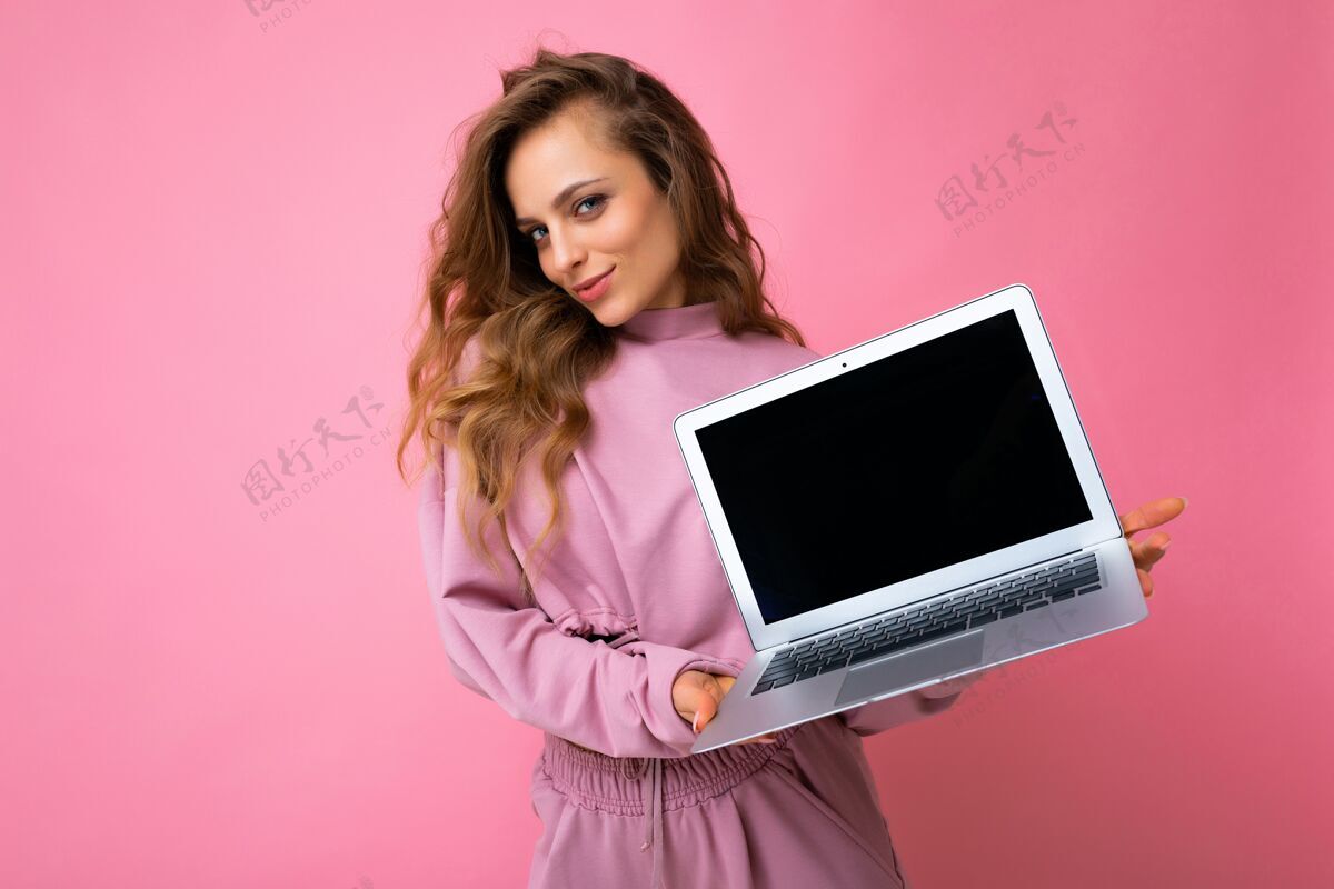 电子一张美丽的金发卷发的年轻女子拿着笔记本电脑看着相机的照片学习蓝牙自由职业者