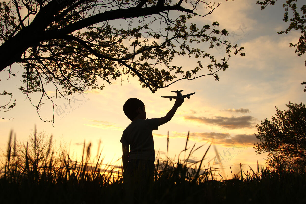 小一个小男孩在美丽的夕阳下手持飞机 象征着世界的和平孩子户外夏天
