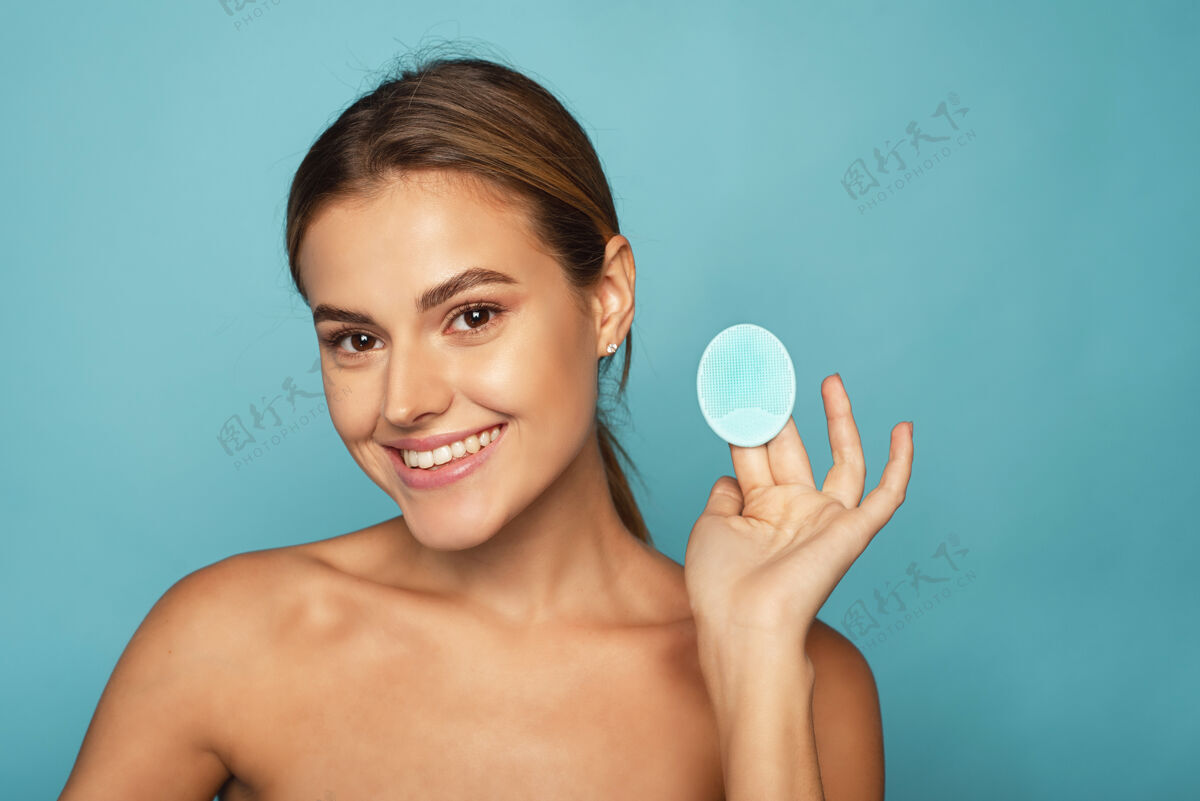 化妆品用硅胶清洁皮肤刷子可爱一位年轻的女士在浴室里用蓝色背景洗去化妆品工作室护肤 洁面 卸妆的概念人清晰美丽
