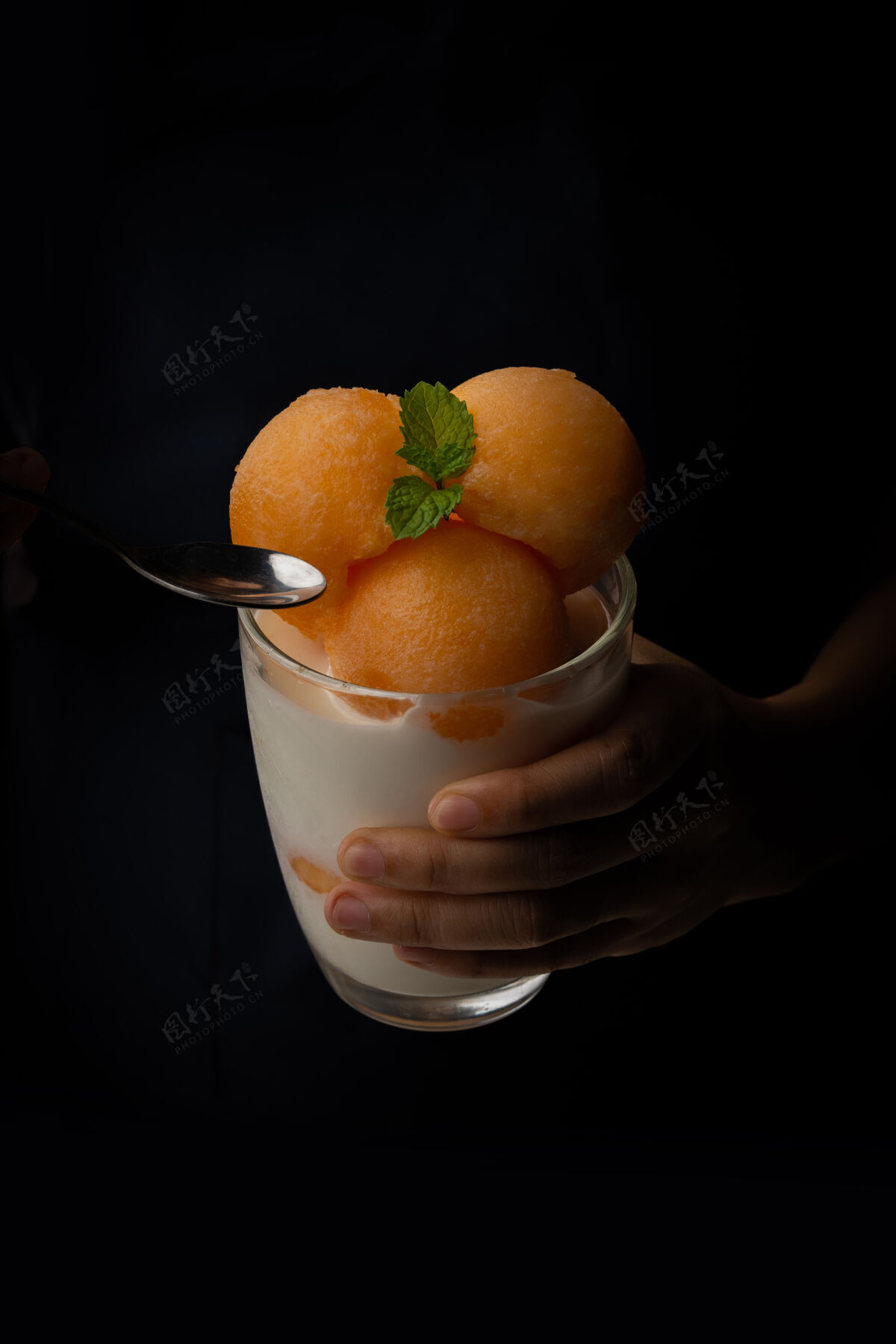 美味黄瓜瓜被舀成一个圆球状 像冰淇淋一样放进一个透明的杯子里 上面放着鲜奶 香甜可口好吃吃吧黑色背景上的照片甜瓜健康切