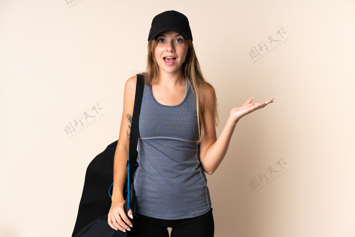 运动年轻的立陶宛运动女子拿着一个运动包孤立在米色背景与震惊的面部表情兴奋力量健身房