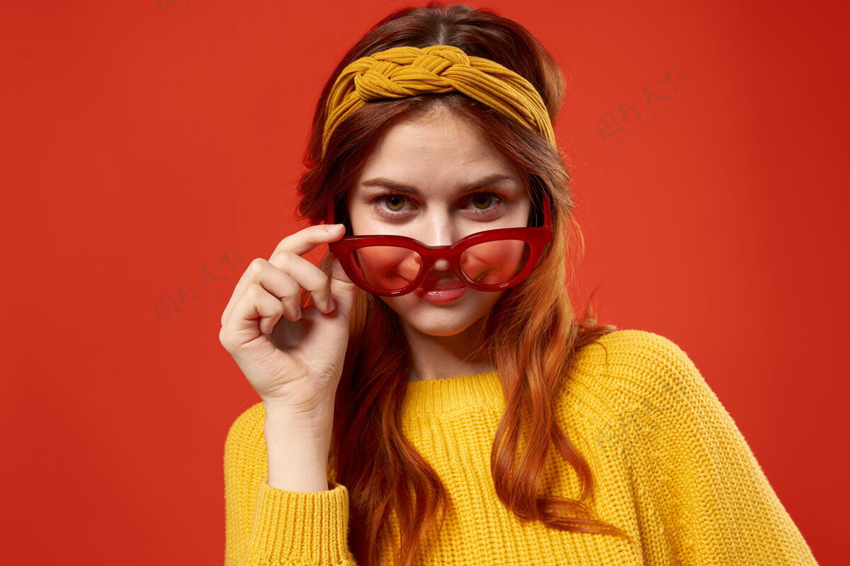 女士穿黄色毛衣的漂亮女人戴着红色眼镜时髦的衣服贴着红墙女性衣服穿着