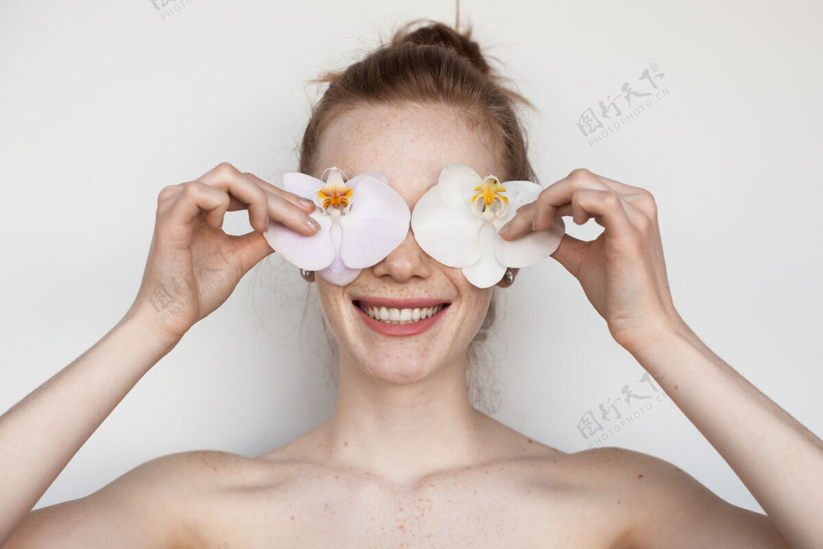 干净的脸一位白人妇女的特写照片 她脱下衣服的肩膀用鲜花遮住眼睛 露出牙齿微笑雀斑姜爱