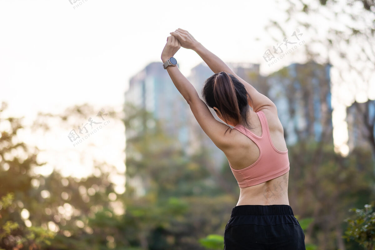 户外穿着粉色运动服的年轻成年女性在公园户外伸展肌肉 运动女性热身准备跑步和慢跑早上好健康 健身 运动和工作生活平衡概念身体健康手