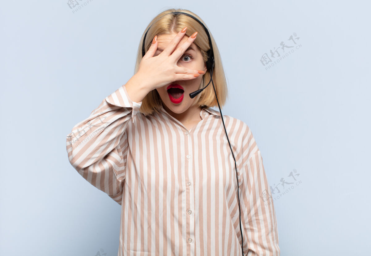 代理金发女人看起来震惊 害怕或害怕 用手捂住脸 用手指偷看耳机呼叫通信