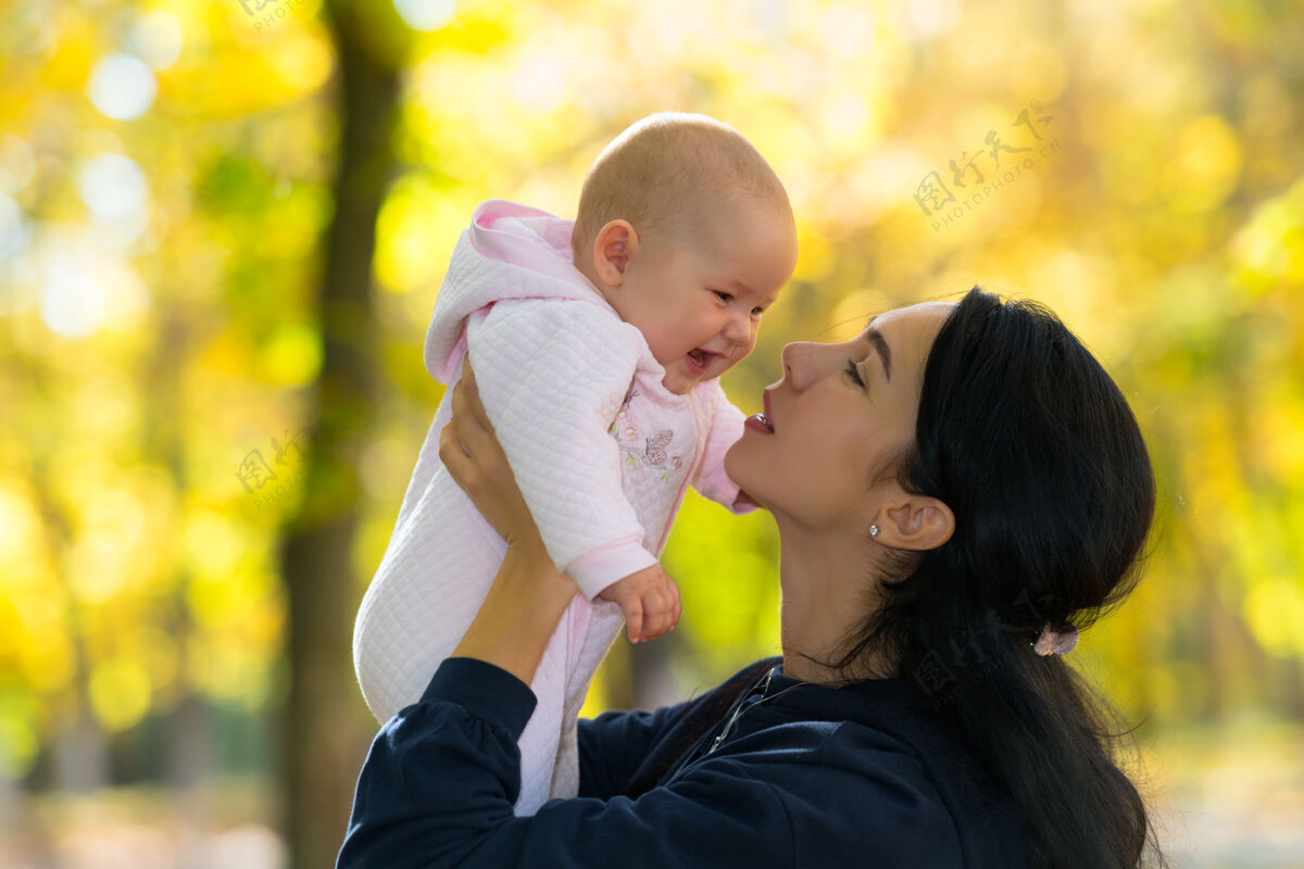 秋天一位慈爱的母亲和她快乐的 欢笑的宝宝在公园里玩耍 景色美丽 秋光明媚树叶乐趣父母