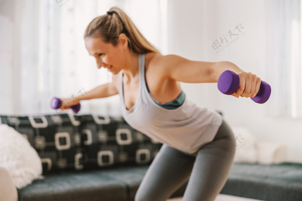 形状微笑肌肉女运动员举起哑铃和做健身操在家里体重锻炼运动装