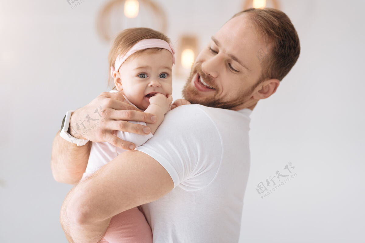 父亲纯粹的快乐可爱和蔼可亲的小女婴躺在年轻父亲的手里 一边看着一边表示积极可爱父母情绪