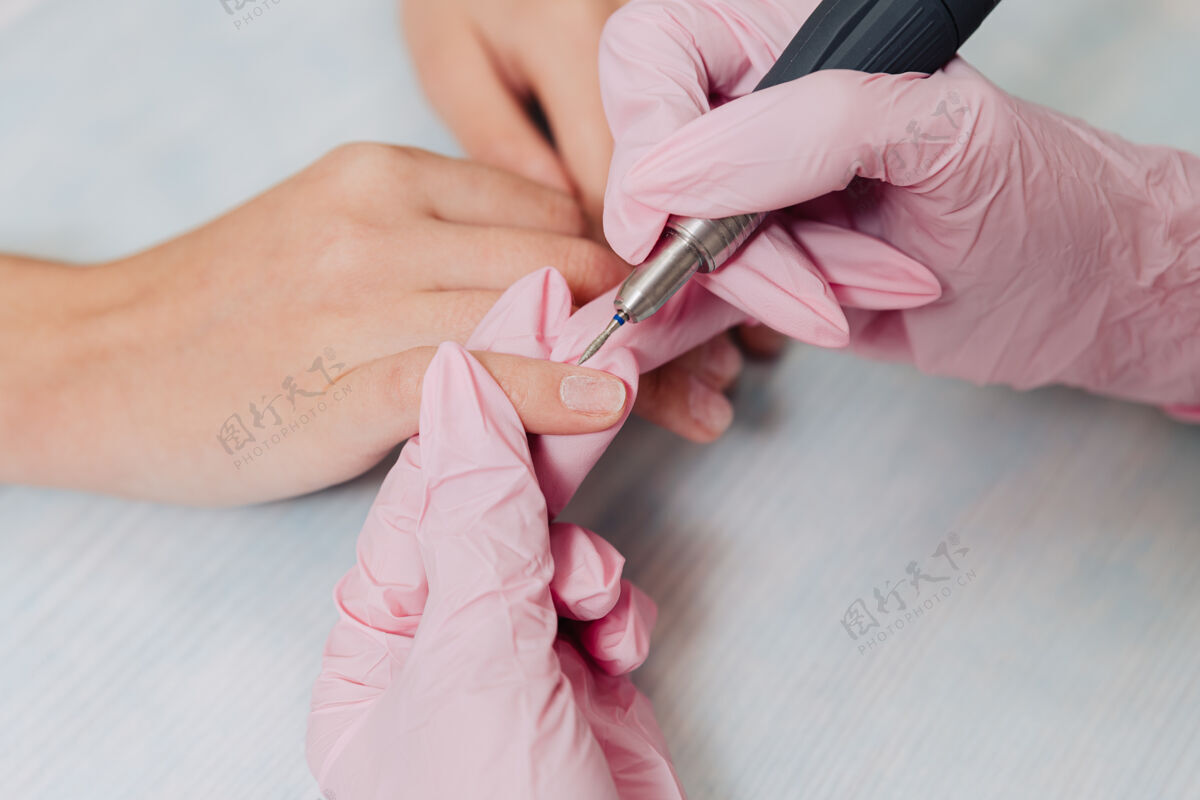 仪器修指甲的过程一位戴着粉色橡胶手套的大师用电动指甲打磨指甲文件.female把手收起来橡胶美容师美甲师