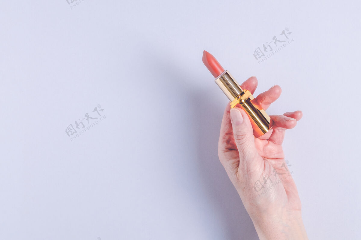 保持一只女性手举着一个亮粉色唇膏在丁香上开着的盒子背景.装饰化妆品概念选择性聚焦 水平方向配件化妆品产品口红