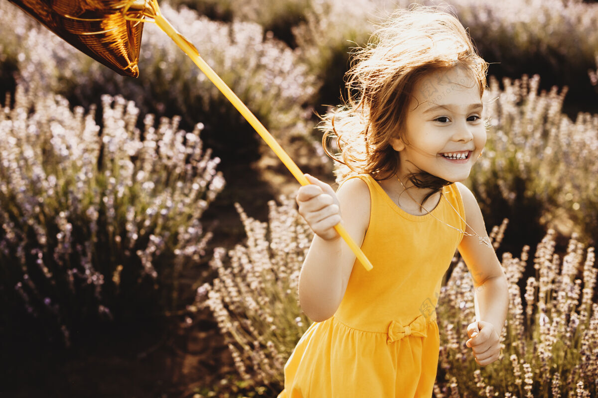 头发一个美丽的小女孩拿着一个金色的气球在花丛中欢笑长草地放松