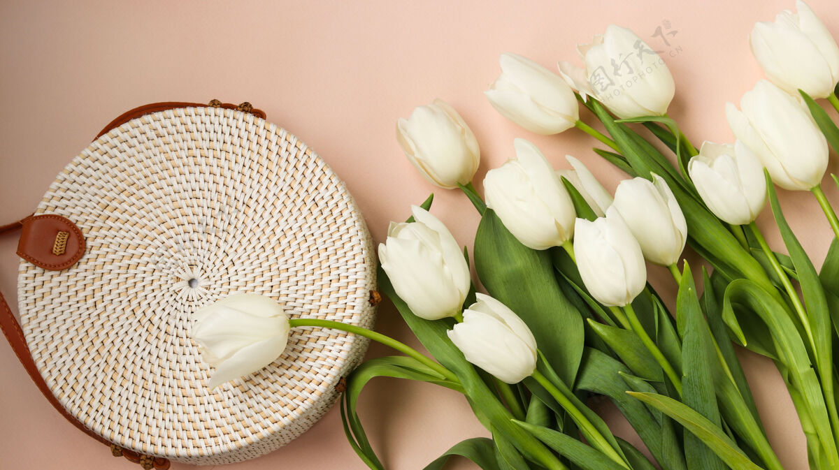 篮子白色郁金香和女士柳条圆形手袋上的粉红色表面 顶视图浪漫顶部花瓣