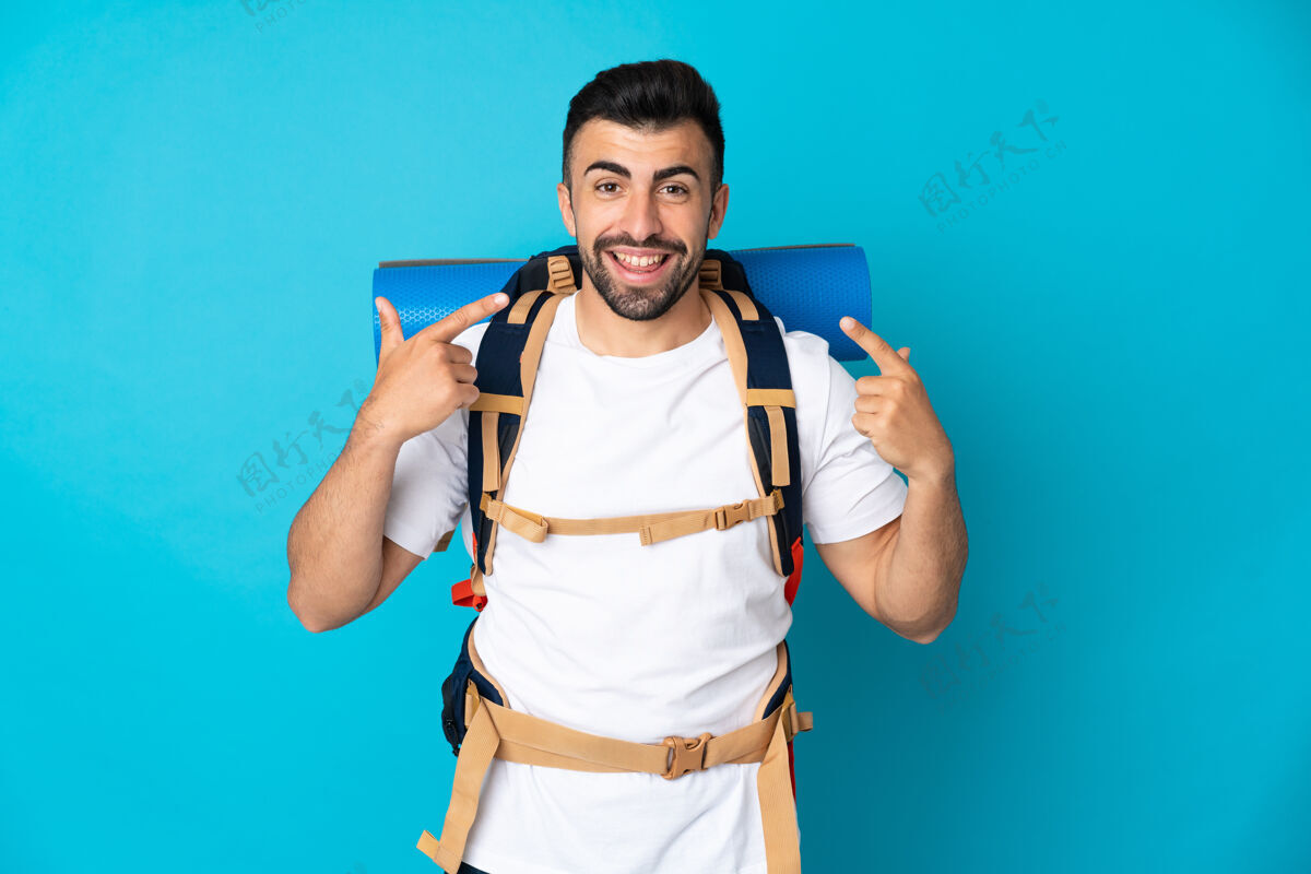徒步旅行者一个年轻的登山者在孤立的蓝色背景上竖起大拇指成人男性旅行者
