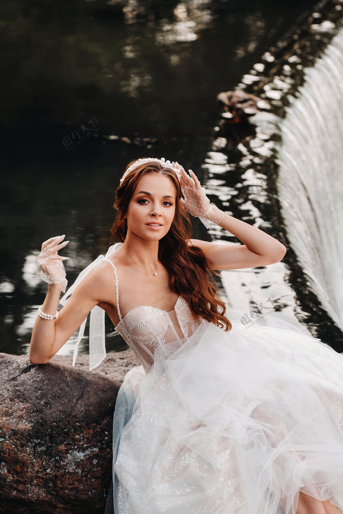 风景一位穿着白色礼服 戴着手套 赤脚的优雅新娘正坐在公园的瀑布旁 享受着大自然手套模型金发
