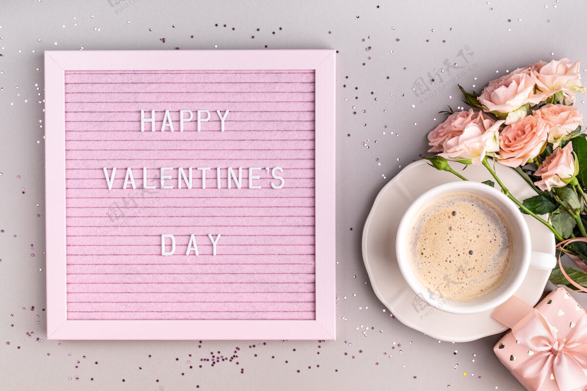 板在咖啡杯和鲜花旁边的粉色毡纸上写着“情人节快乐”字样礼物形状浪漫