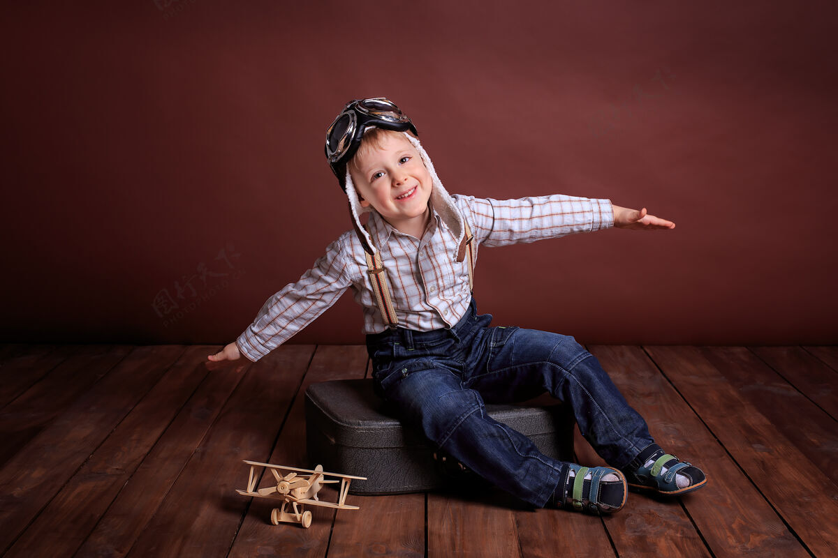 飞机一个戴着飞行员头盔的小男孩和一个木头玩具玩飞机男孩穿着格子衬衫和吊带帽子苍蝇航空