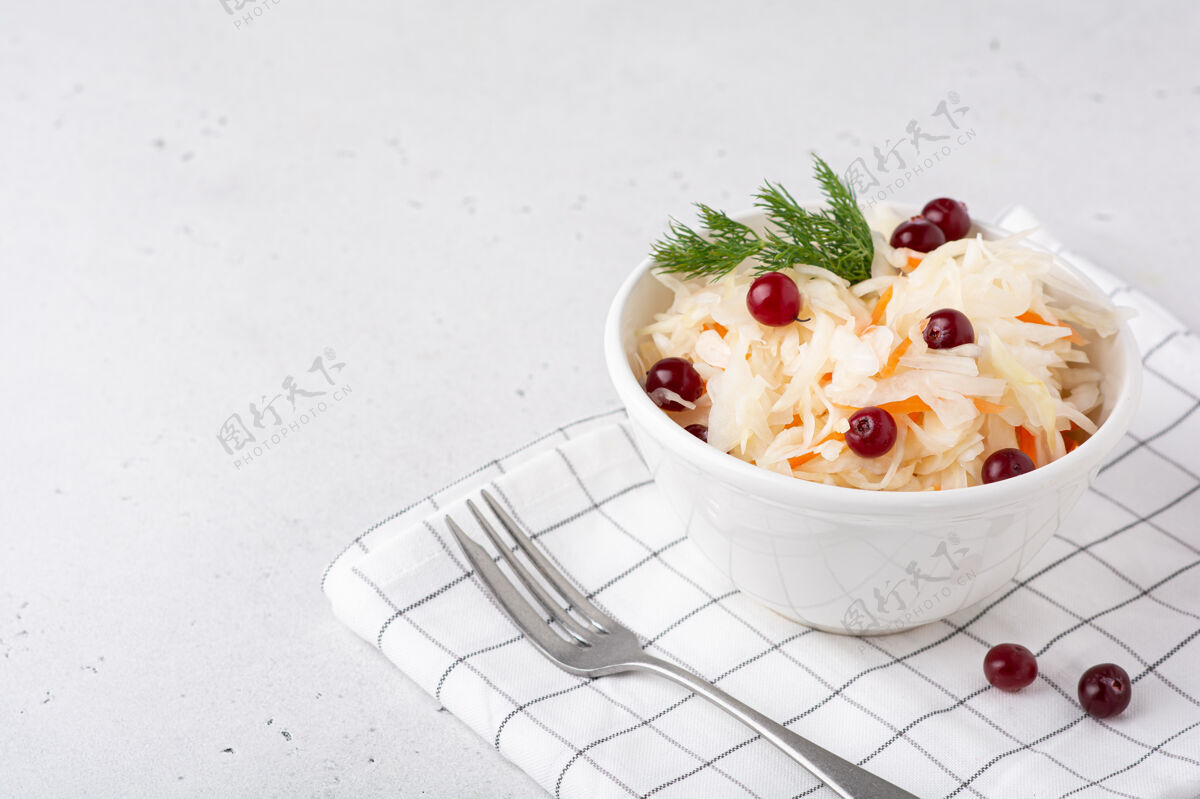 蔬菜酸菜和酸果蔓放在一个白色的陶瓷碗里 放在一张浅色的桌子上 放上文字健康发酵泡菜