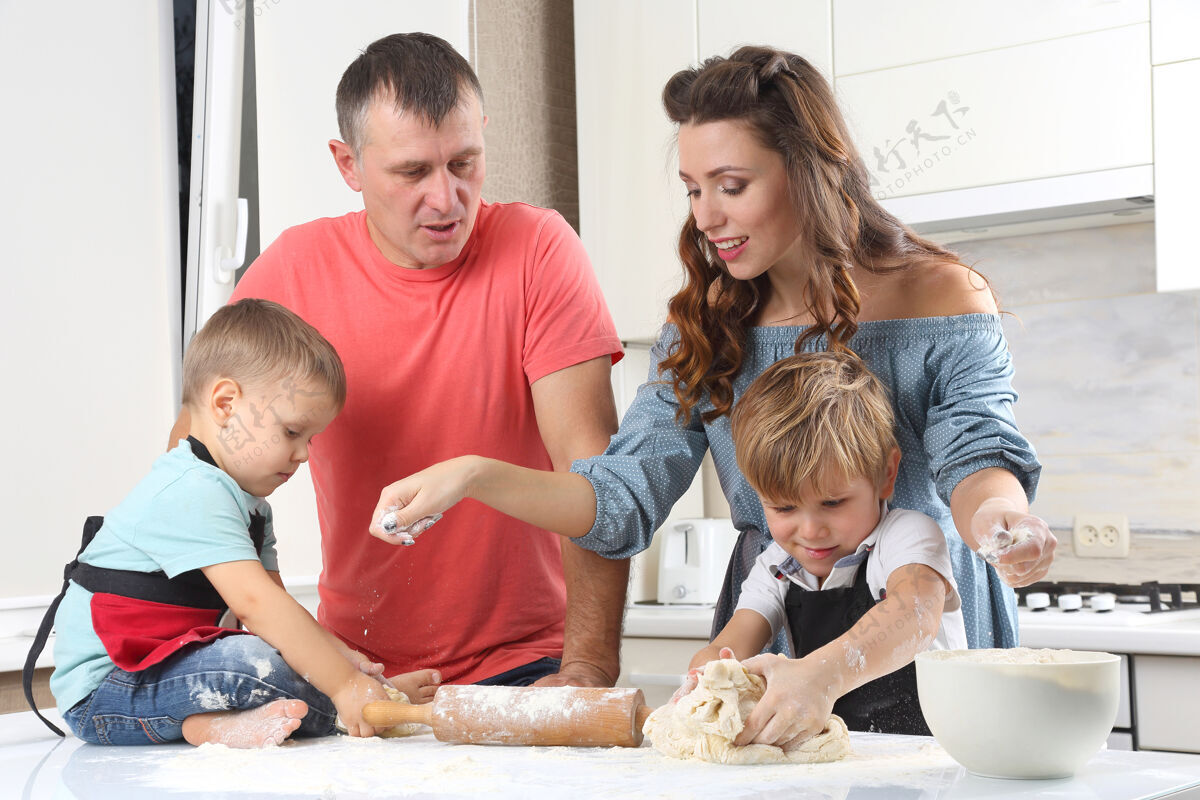 微笑年轻的父母坐在厨房桌子上揉面团的小孩子旁边团队合作面包师烹饪