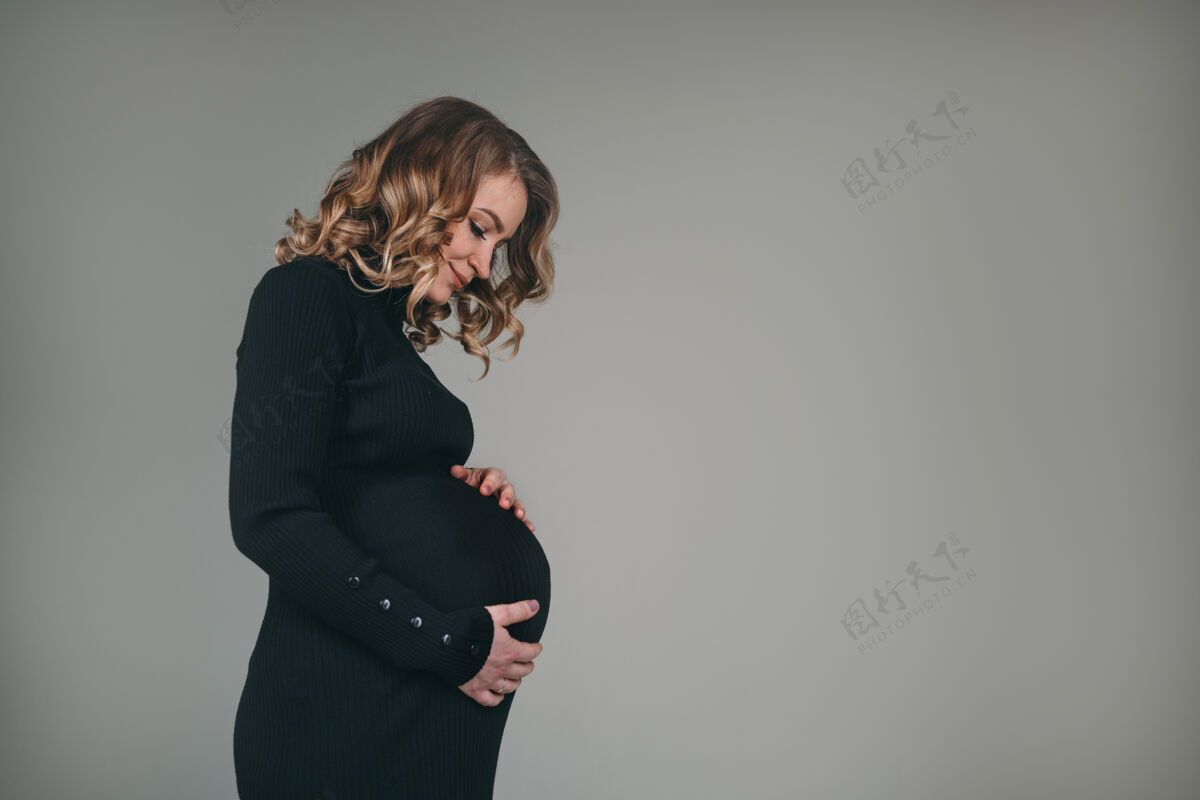 积极一个穿着黑色连衣裙的怀孕的漂亮女孩一个女人正期待着一个孩子的诞生护理腹部产妇