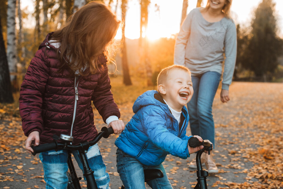 自行车一个可爱的小孩在公园里骑着自行车和她的妹妹在夕阳下玩耍时大笑的画像父母儿子关系