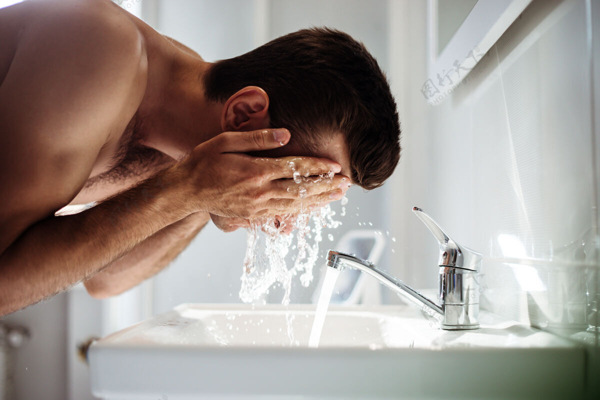 成人帅气的年轻裸男在家的浴室里洗脸飞溅干燥家庭