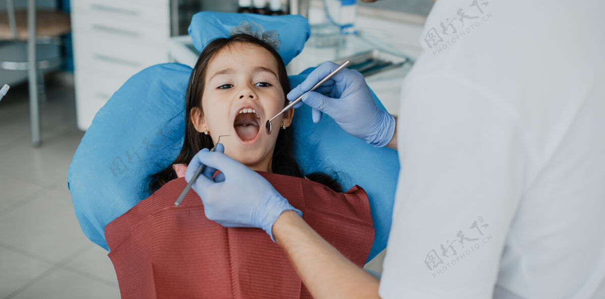 牙齿可爱的小女孩正在接受儿科口腔医生的牙齿手术椅子诊所制服
