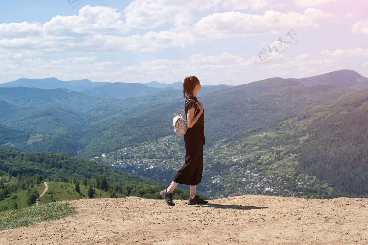 天空背着背包的女孩站在山上欣赏着视图.阳光天哪后方美丽假期