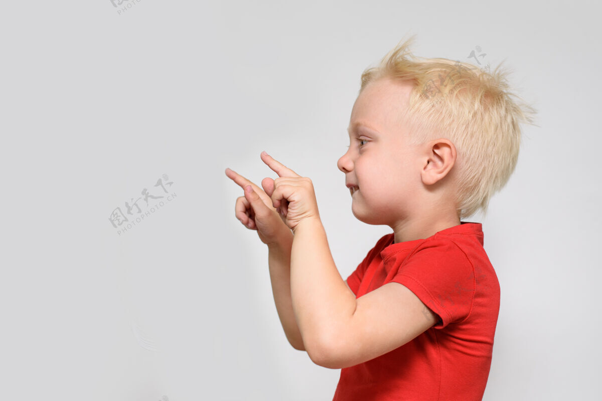 年轻穿红色t恤的金发小男孩指着他的手手指空间为了文本位置为了广告白色背景指向文字可爱