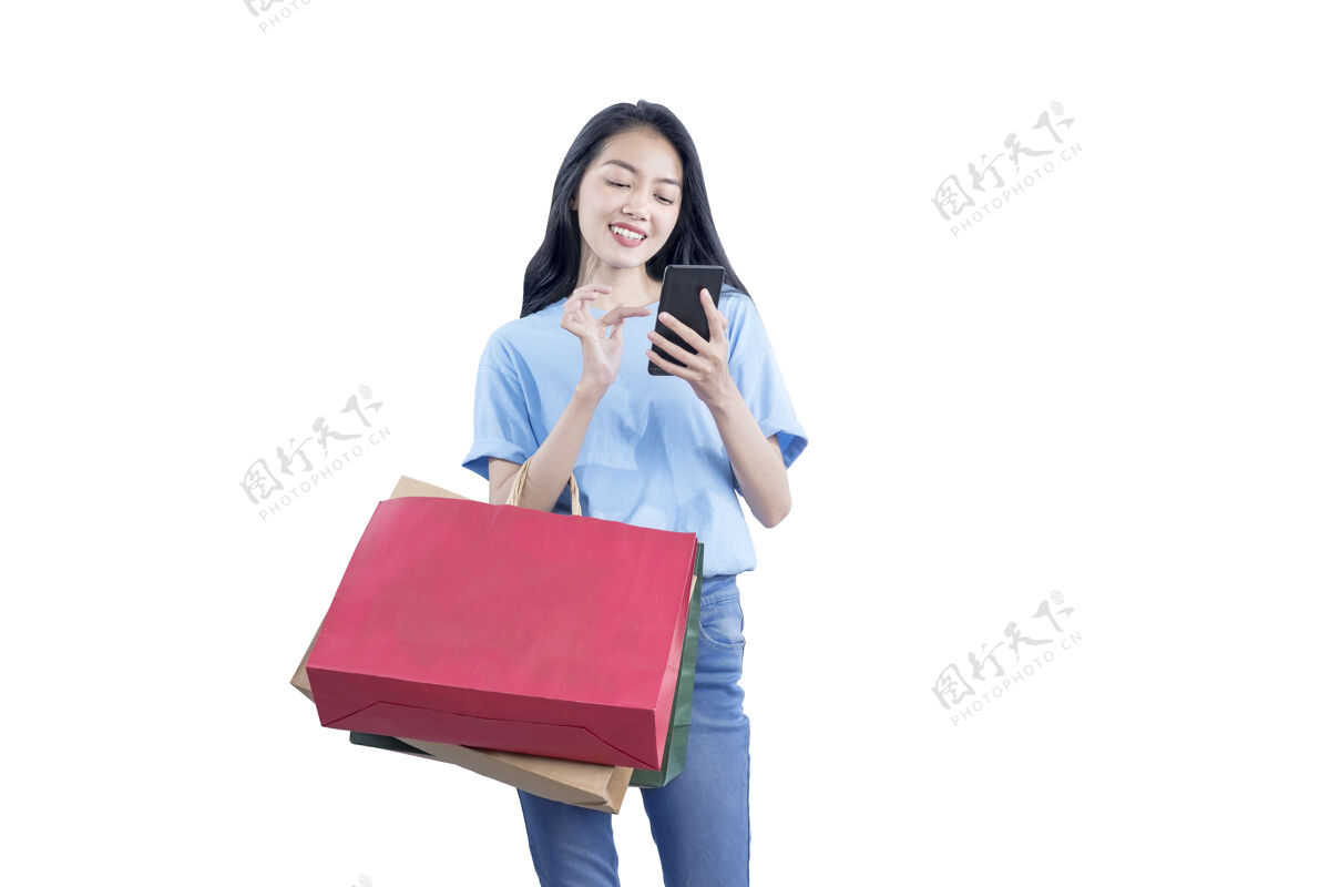 消费主义亚洲女人拎着购物袋拿着手机隔着白墙包泰国携带