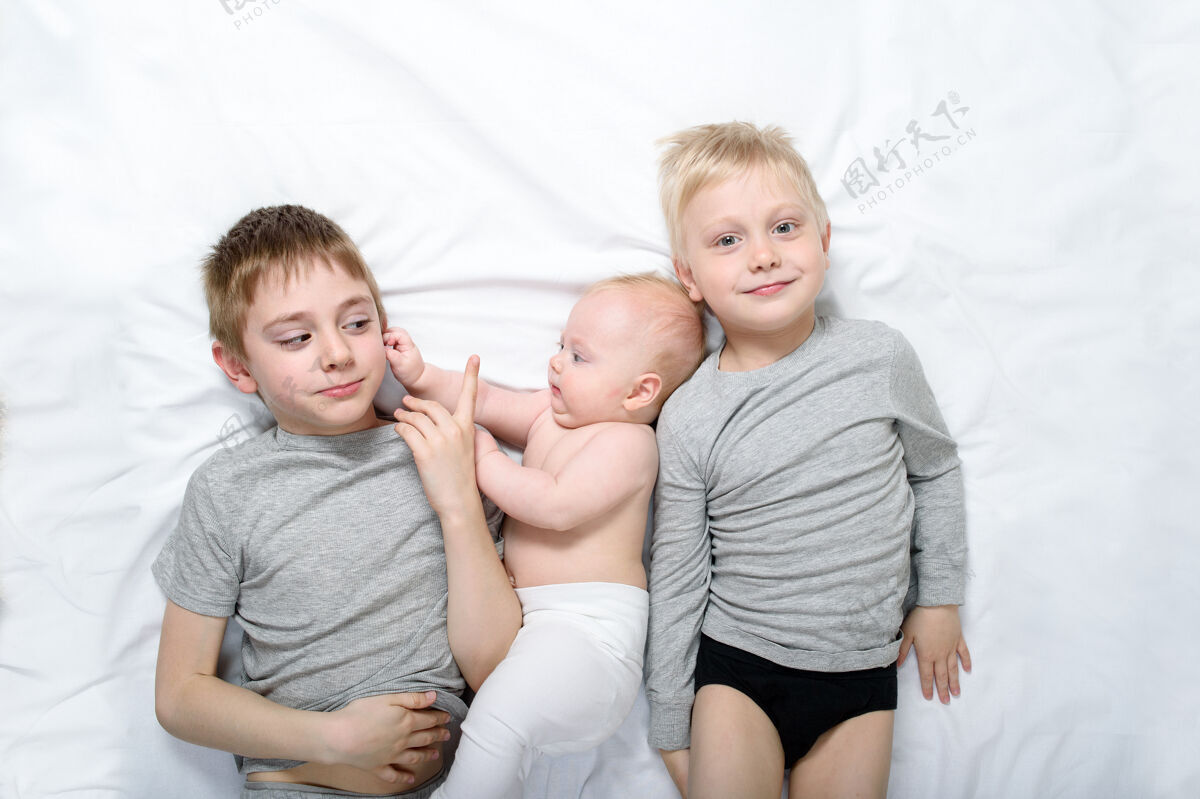 近距离两个哥哥和穿白色衣服的最小的婴儿一起嬉笑床快乐童年 大家庭在一起姐妹可爱