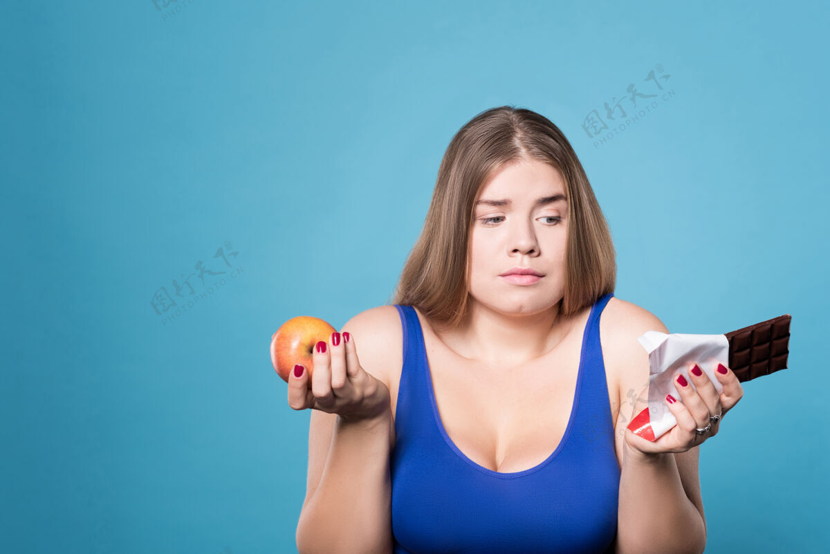 过量硬的决策.肖像一个手里拿着苹果 另一只手里拿着巧克力的年轻女人女人身材食物