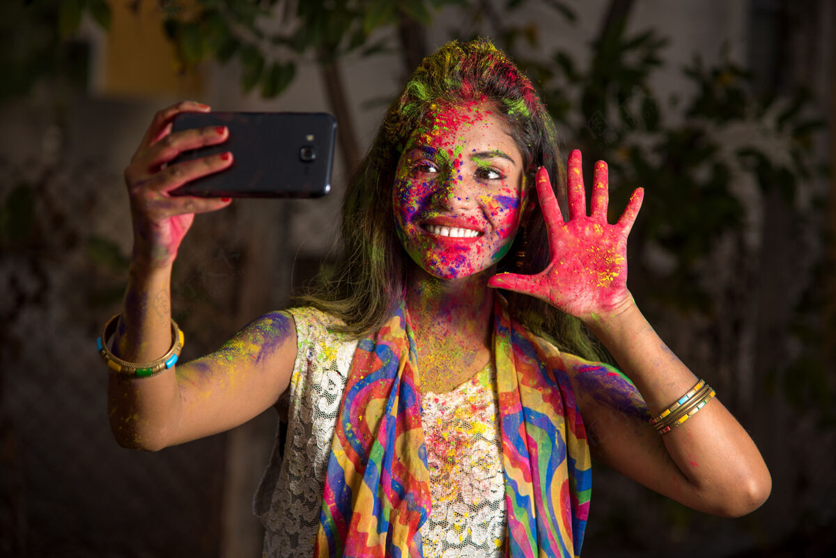 快乐在胡里节上用智能手机拍彩色脸的年轻女孩绘画年轻印度