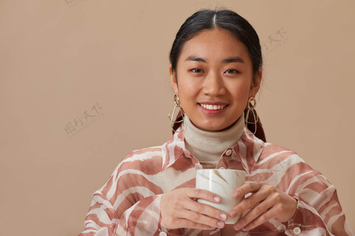 室内照片中的亚洲年轻女子正拿着茶杯微笑 茶杯被隔离在米色的墙上喝酒微笑咖啡休息