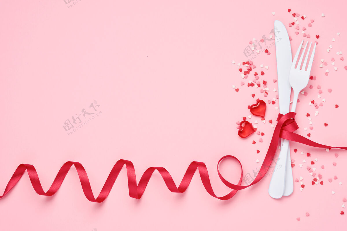 地点情人节午餐的背景或概念菜单.餐具白色的刀叉与红色的丝带和小小的心交织在一起宴会银器事件