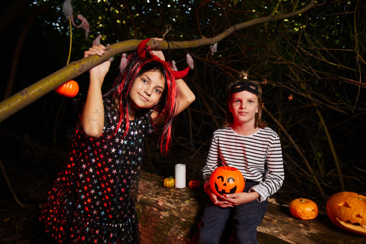 庆祝两个女孩的肖像 而坐在户外在黑暗中万圣节派对女巫服装南瓜