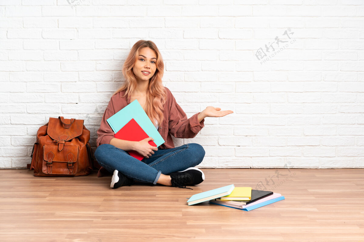 女性一位粉红色头发的女学生坐在室内的地板上 向侧面伸出双手 欢迎前来坐着全长大学