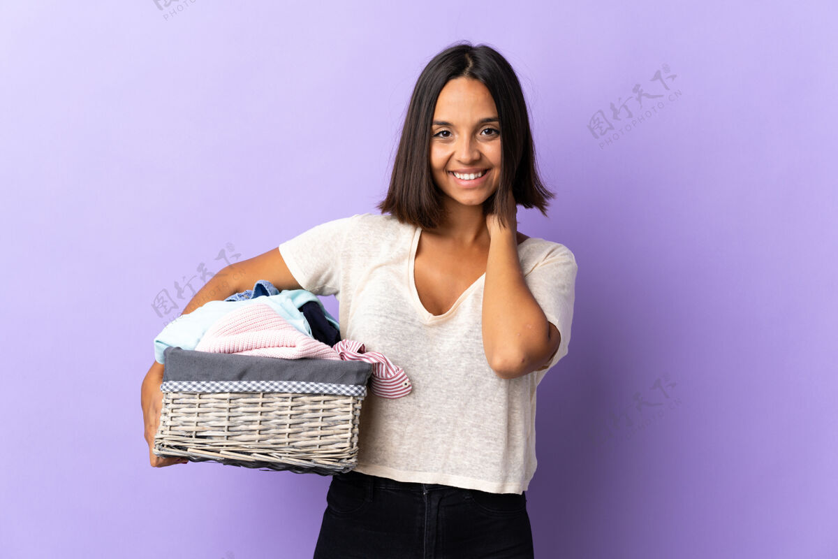 姿势年轻的拉丁女子拿着一个衣篮孤立地笑着对紫色脏湿手臂