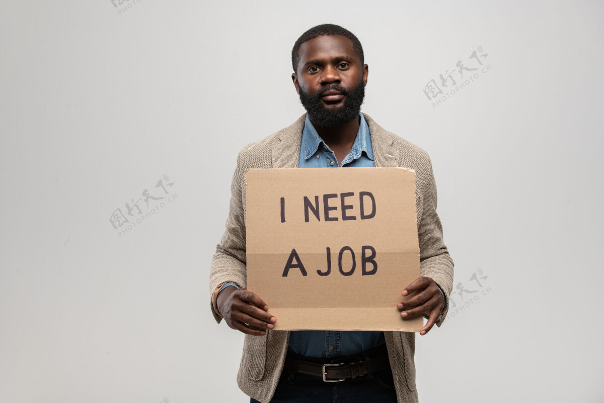 求职非洲裔的年轻无业男子穿着正装 站在办公室里拿着一张纸板说他需要一份工作投票白领概念