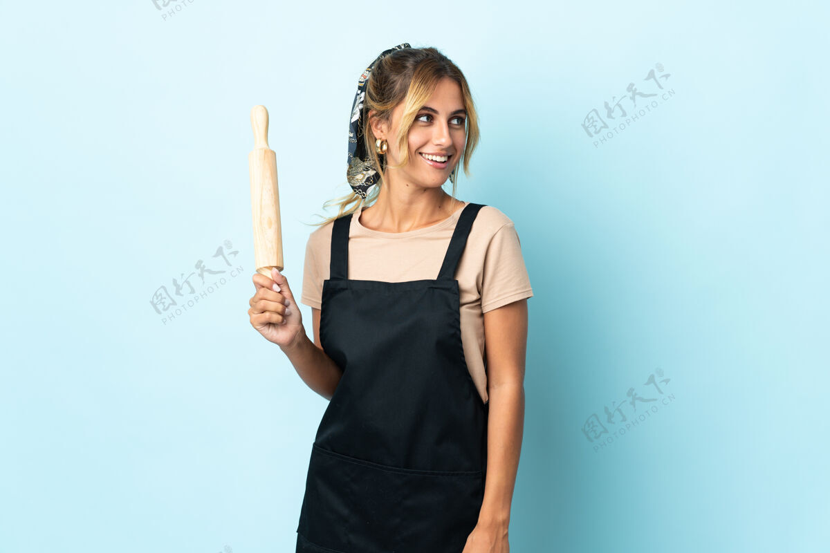 金发年轻的金发乌拉圭厨娘孤立在蓝色的一面面包房厨师别针