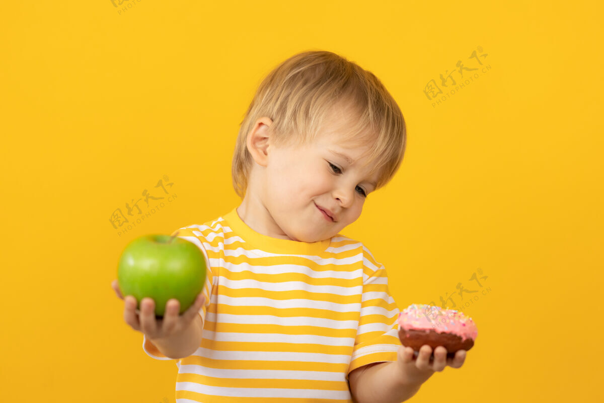 快餐快乐的孩子拿着甜甜圈和苹果选择食品素食主义者
