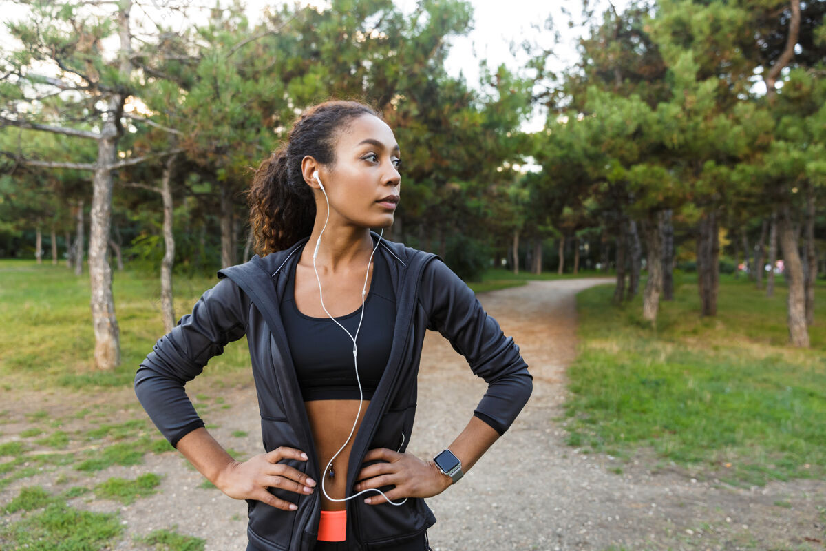 黑发20多岁的健康女性穿着黑色运动服 戴着耳机 在绿色公园里跑步跑步成人身体