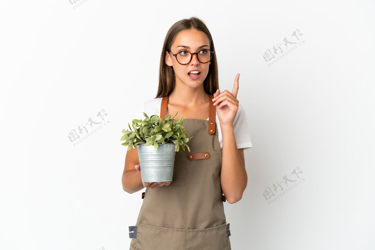 怀疑园丁女孩拿着一株植物在孤立的白色背景上思考着一个想法 手指向上花园思考表达