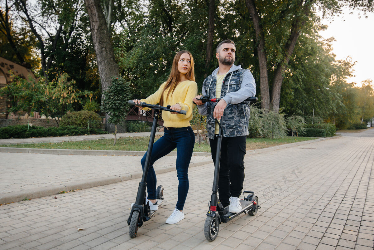 踏板车在一个温暖的秋天 一对年轻漂亮的夫妇在公园里骑着电动滑板车爱好和娱乐骑道路踏板车