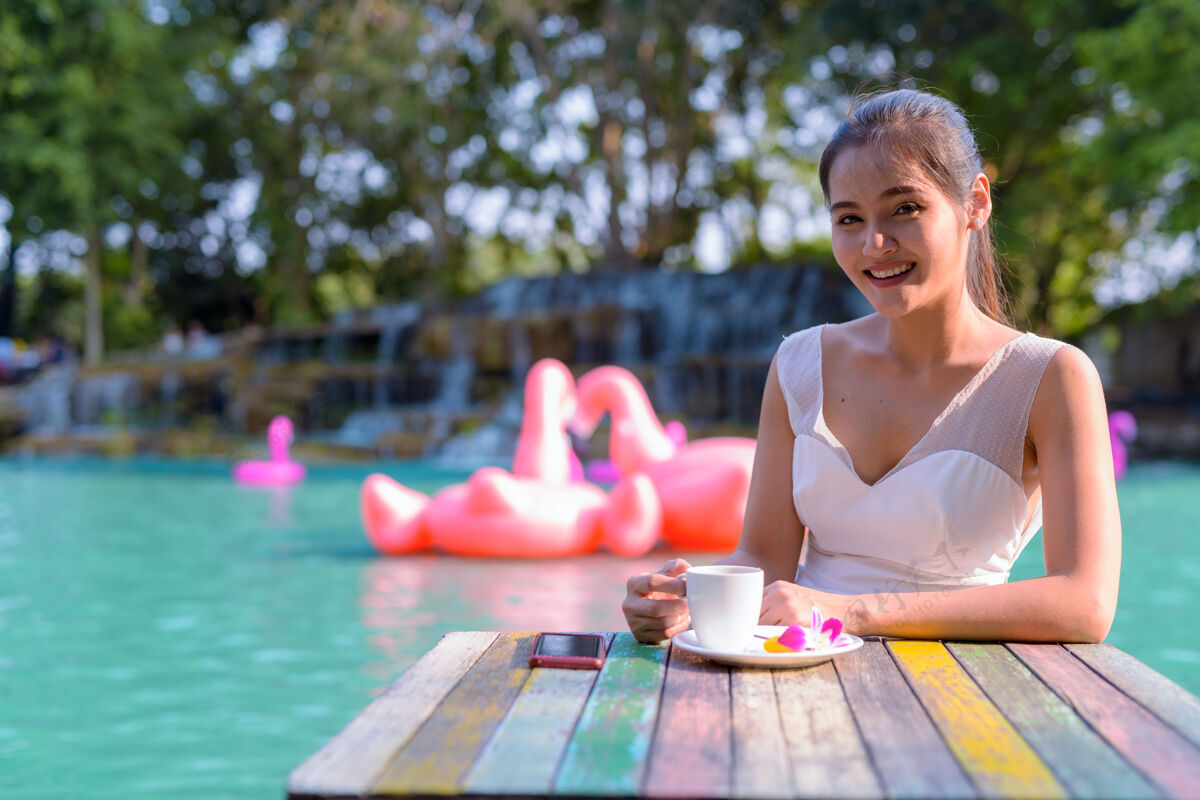 咖啡因年轻美丽的亚洲女游客在湖边户外放松的画像微笑公园年轻